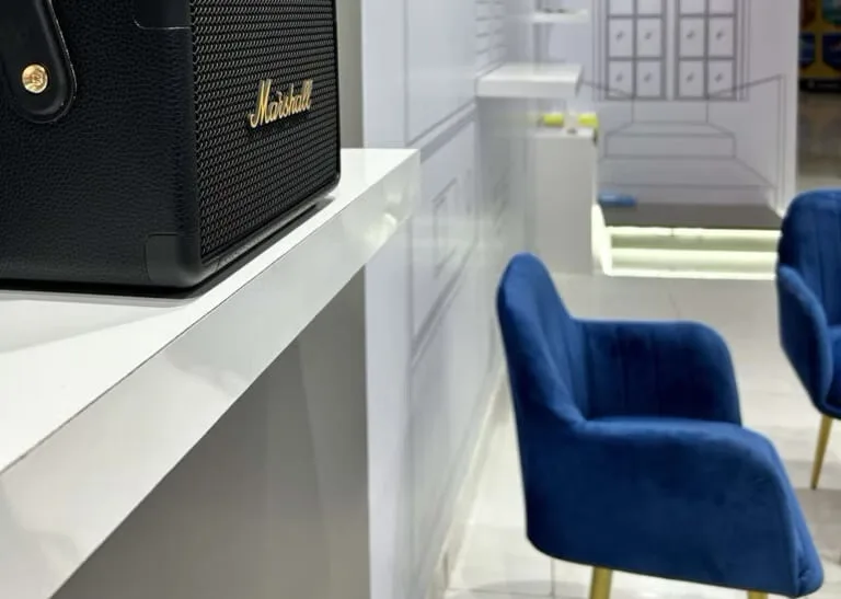 A speaker on a white display shelf in the finished showroom, blue velvet seating and pale joinery beyond