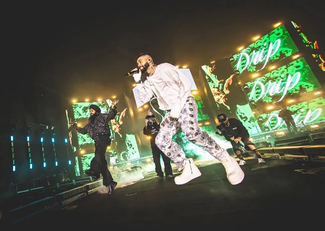 The artist mid-motion in white, green lettering running across the LED panels behind